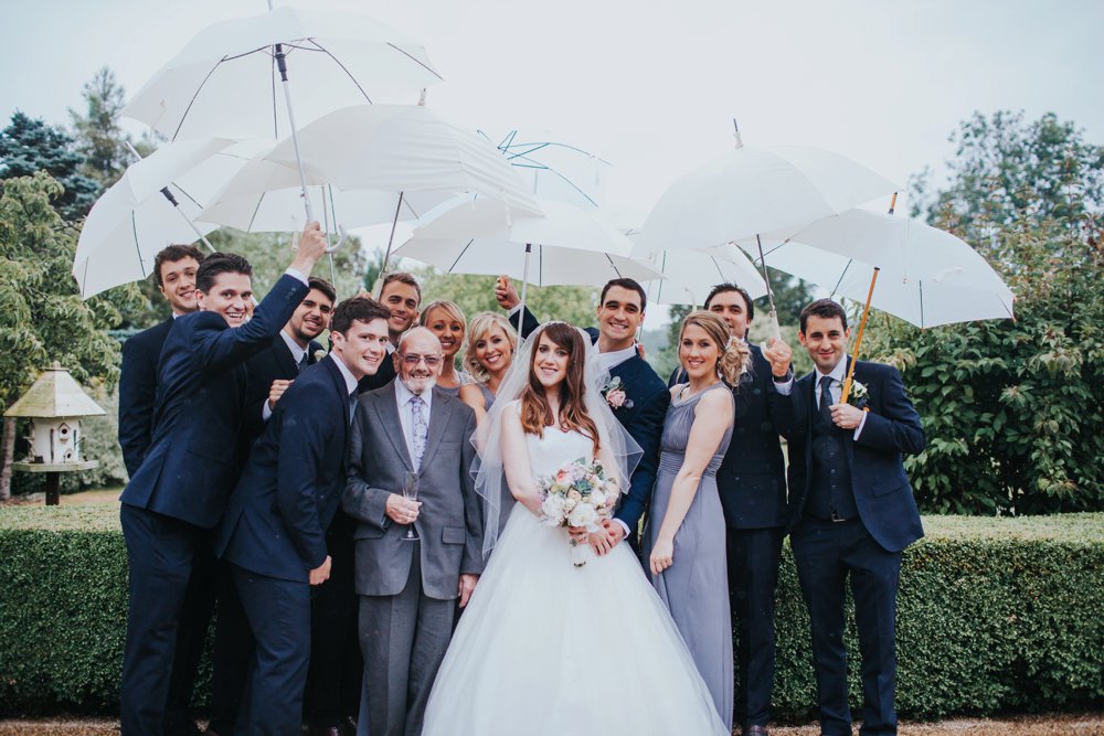 bride and groom standing in the rain with umbrellas