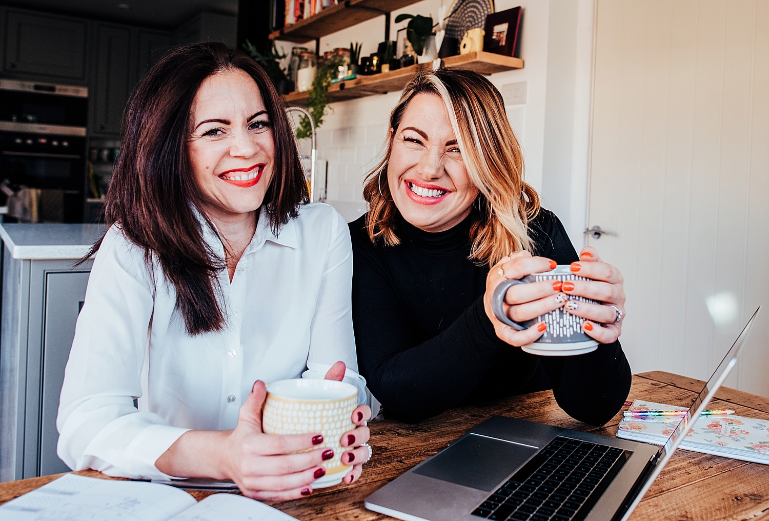 two working women sitting at bench smiling holing cup of tea